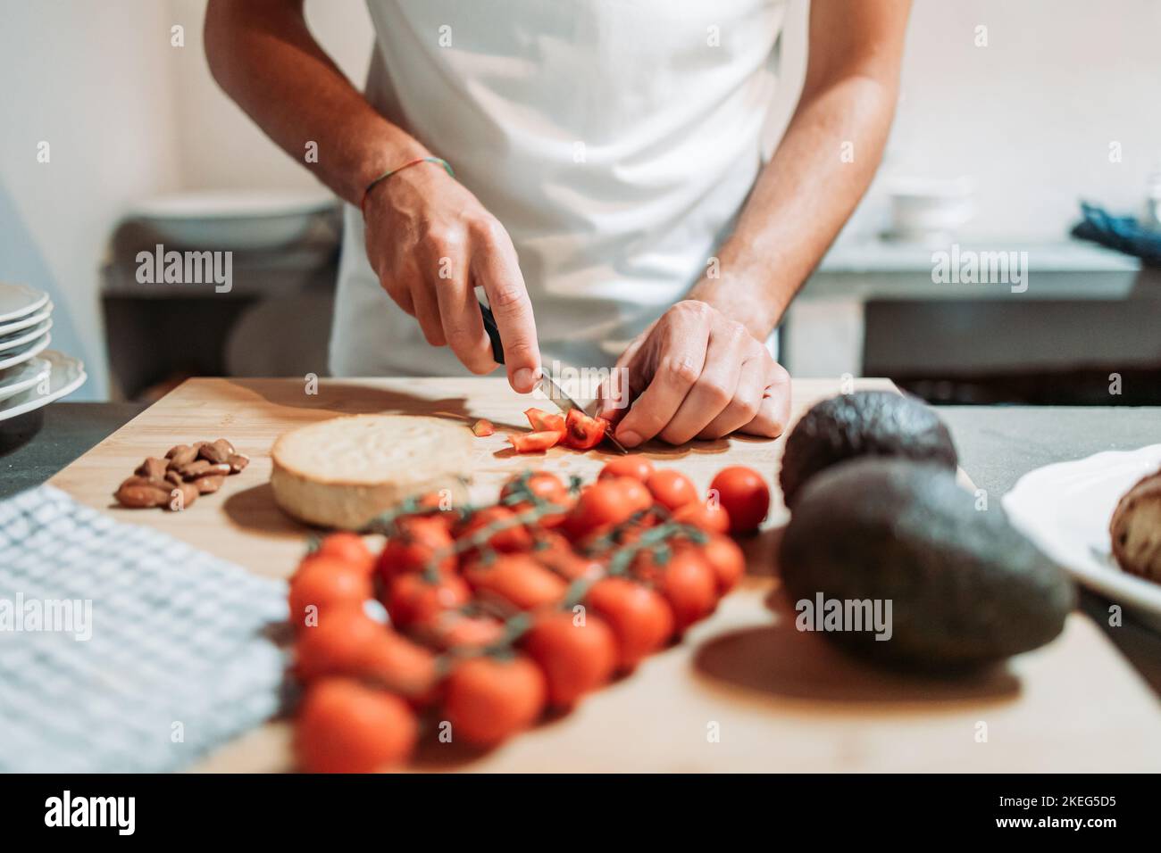 Männliche Hände schneiden Kirschtomate auf dem Küchenbrett. Salatzubereitung. Gesunde Ernährung Stockfoto