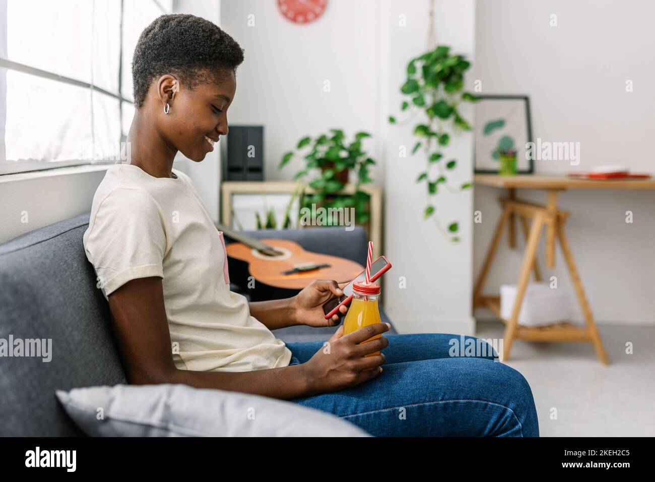 Junge Erwachsene afrikanerin, die ein Mobiltelefon benutzt, während sie sich zu Hause auf dem Sofa entspannt Stockfoto