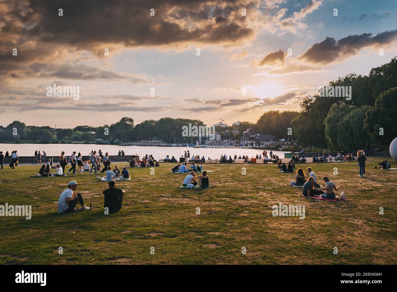 25. Juli 2022, Münster, Deutschland: Menschen, die sich im Stadtpark von Münster ausruhen und den Sonnenuntergang über dem Aasee beobachten Stockfoto