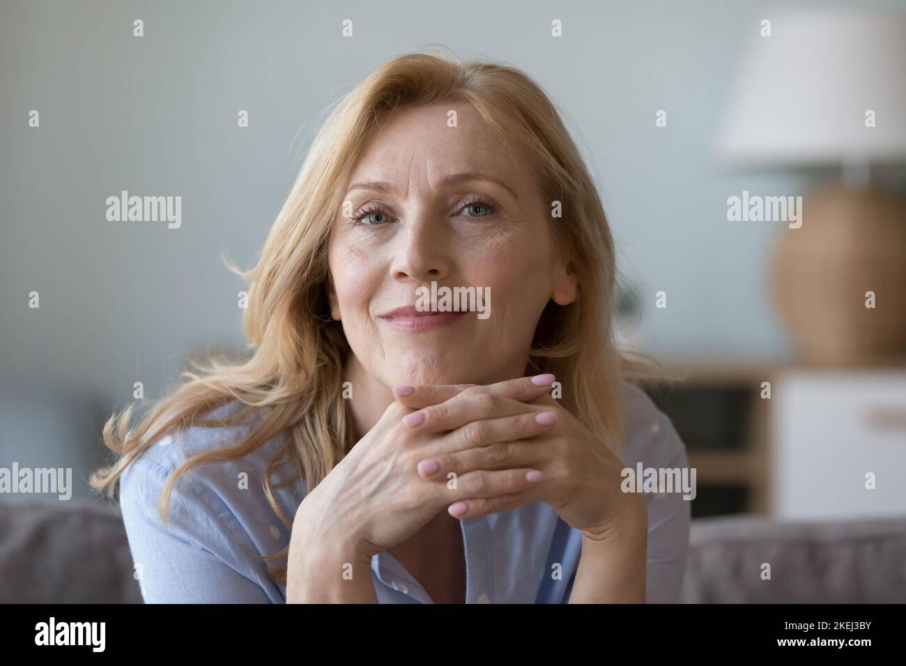 Attraktive Frau mittleren Alters, die sich auf dem Sofa ausruht, schauen Sie sich die Kamera an Stockfoto