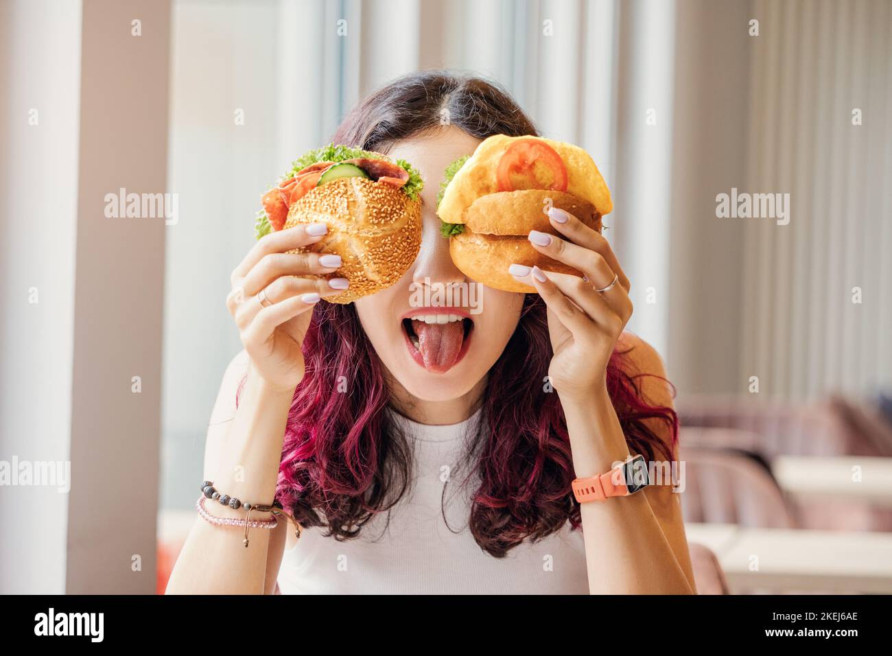 Ein Mädchen in einem Café dummte herum und schloss ihre Augen mit zwei Cheeseburgern. Fast Food und gesunde Ernährung Konzept Stockfoto