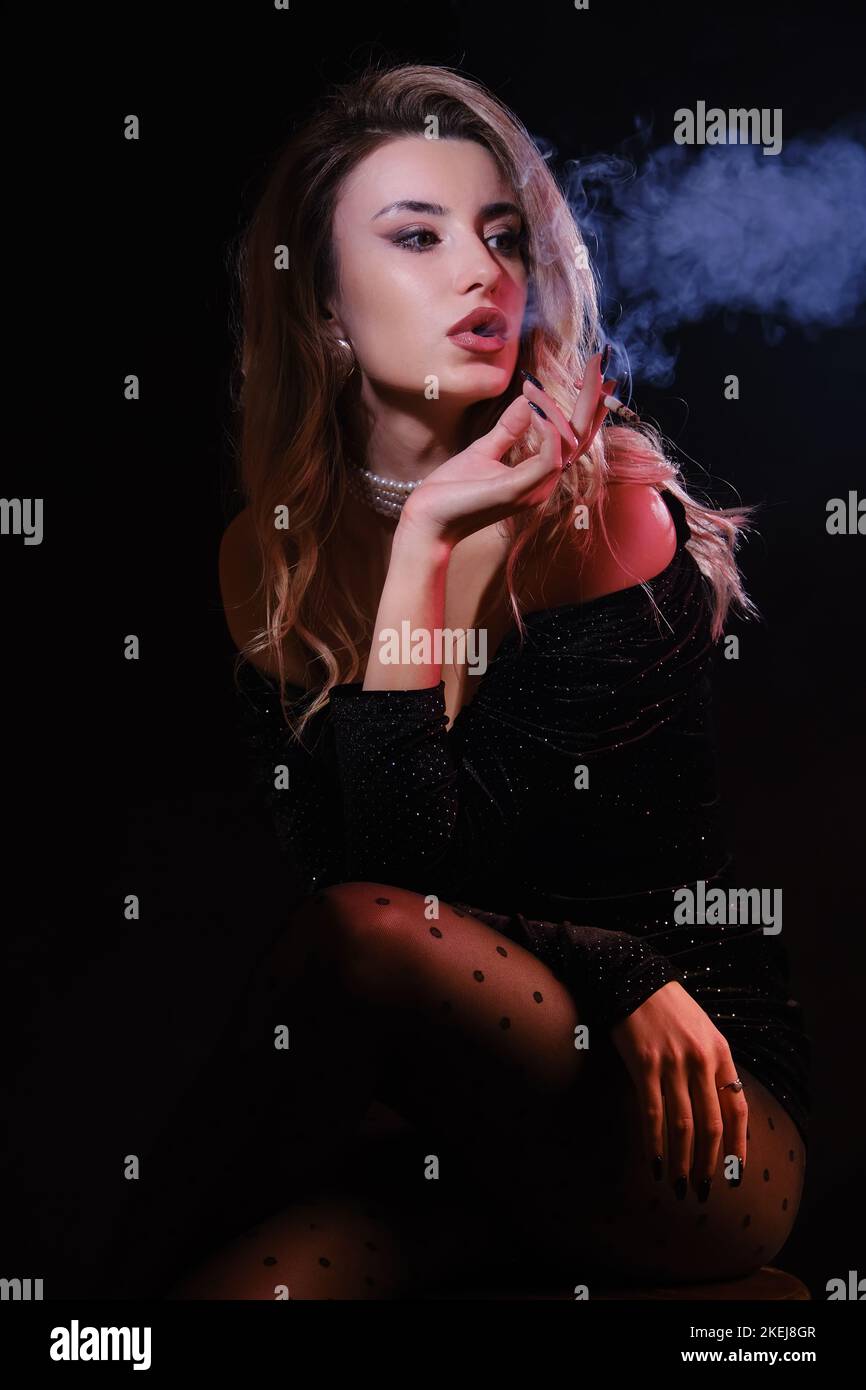 Luxusfrau in schwarzem Kleid mit Dekolleté, die Zigarette raucht, auf schwarzem Hintergrund Stockfoto