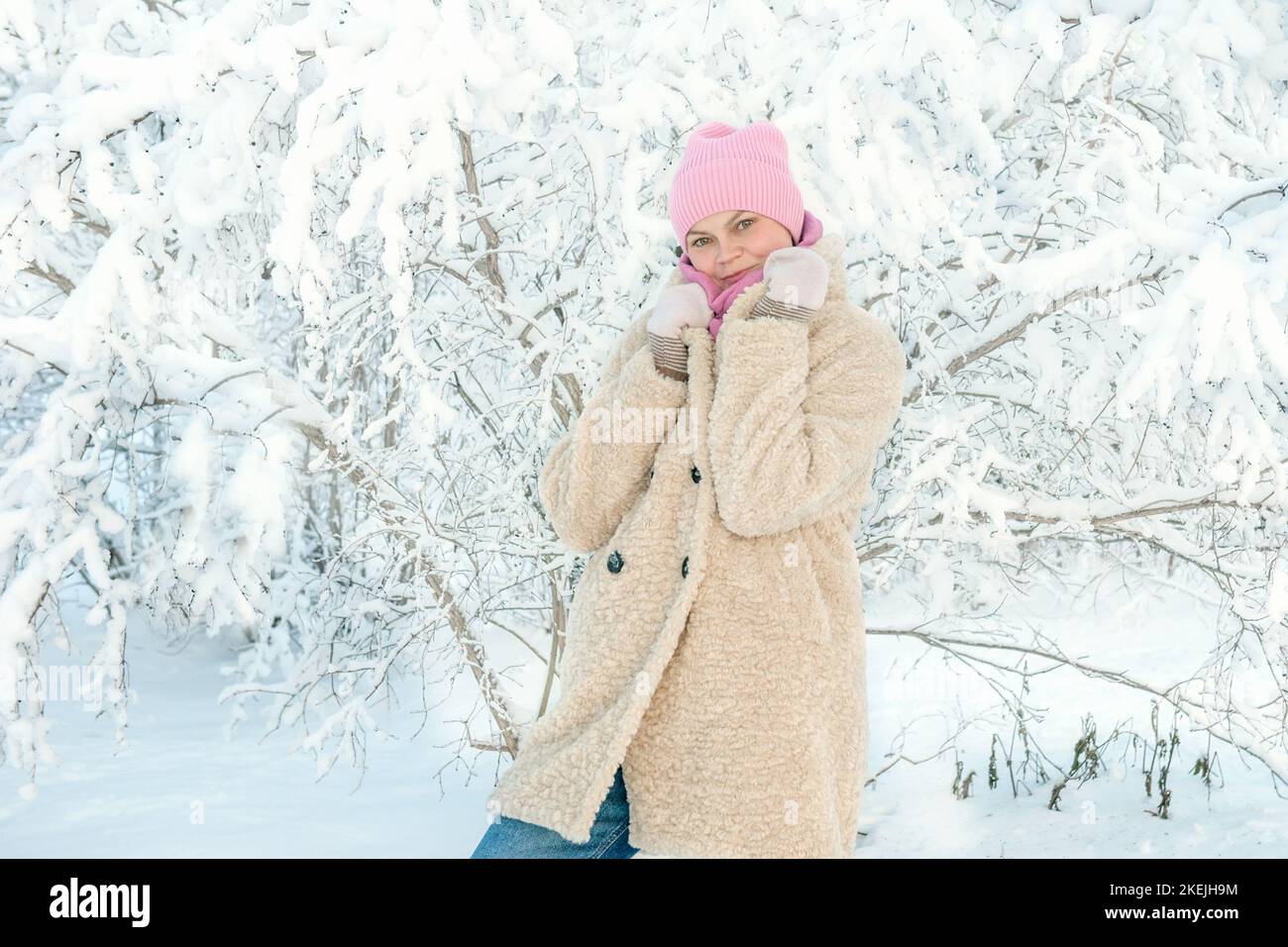 Junge Frau auf dem Hintergrund einer schönen Pflanze im Schnee. Eine junge Dame berührt bei einem Schneefall einen Ast im Schnee. Tolle Stimmung, Freude, Spaß. Stockfoto