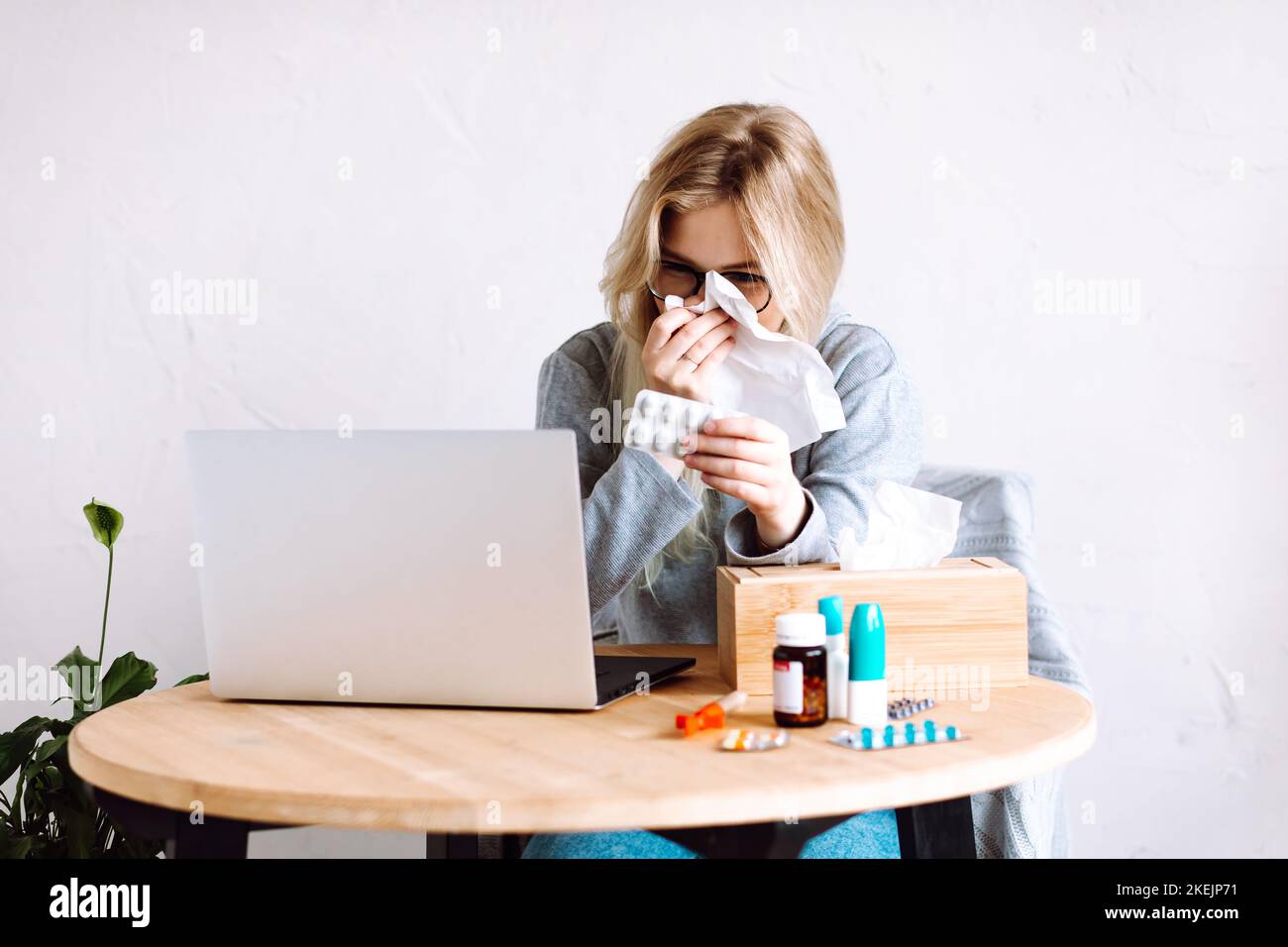 Porträt einer jungen Frau, die Pillen Blister auf Bildschirm zeigt, laufende Nase mit Serviette wischend, Arzt online konsultieren. Stockfoto