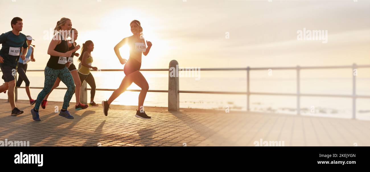 Fit Menschen laufen ein Marathon-Rennen entlang einer Promenade am Meer. Läufer und Läuferinnen treten bei einem Lauf an, fördern aber gleichzeitig einen gesunden Lebensstil und ein Stockfoto