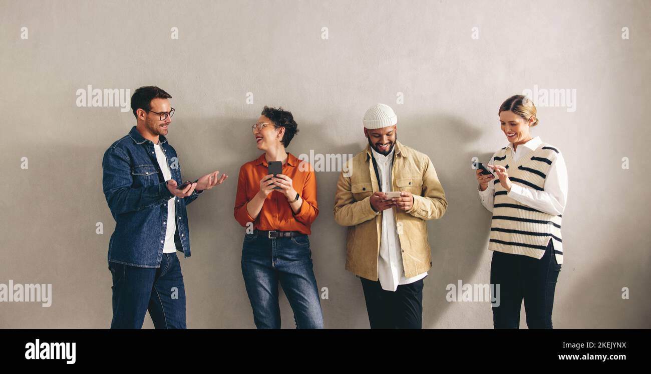 Glückliche Geschäftsleute, die in einem Wartebereich stehen, chatten und ihr Smartphone nutzen. Gruppe von Kandidaten in der engeren Auswahl, die sich auf eine Stelle einlassen intervi Stockfoto