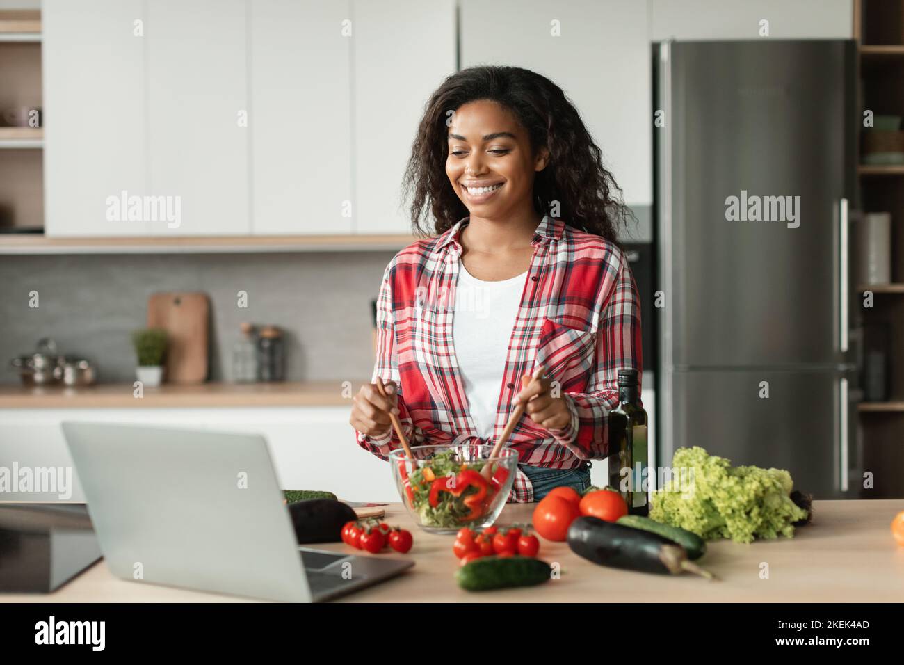 Glad schwarze junge Dame in Casual bereitet Salat aus Bio-Gemüse und Video-Lektion des Rezepts Stockfoto