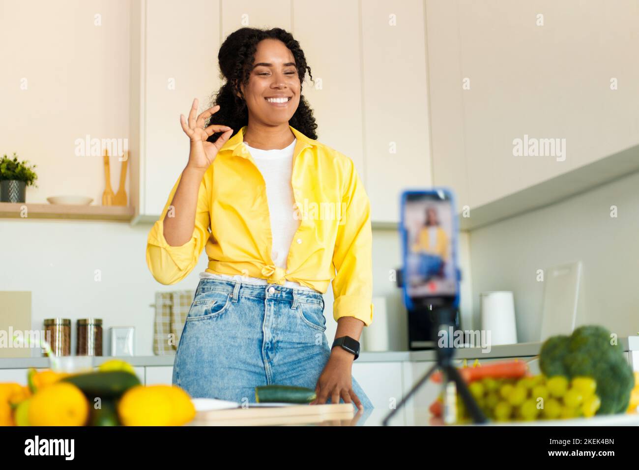 Bloggen von Lebensmitteln. Aufgeregt schwarze Frau schießen auf Handy in der Küche, Kochen und Aufnahme von Video, gestikulieren ok Stockfoto