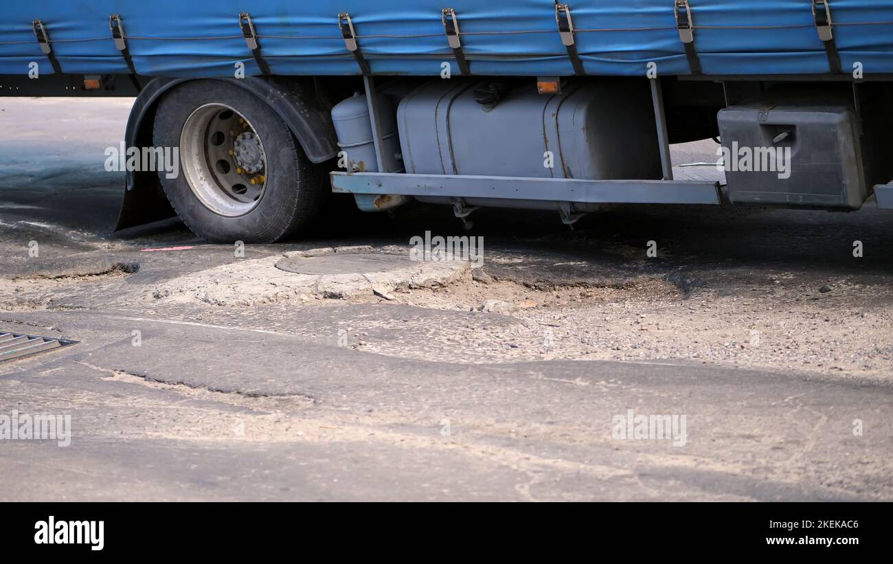 Nahaufnahme, sehr schlechte Straßenabdeckung, viele Gruben, gekrümmter Asphalt, ein großer LKW passiert langsam ein Stück Straße in Verfall. Die Straße muss repariert werden. Hochwertige Fotos Stockfoto