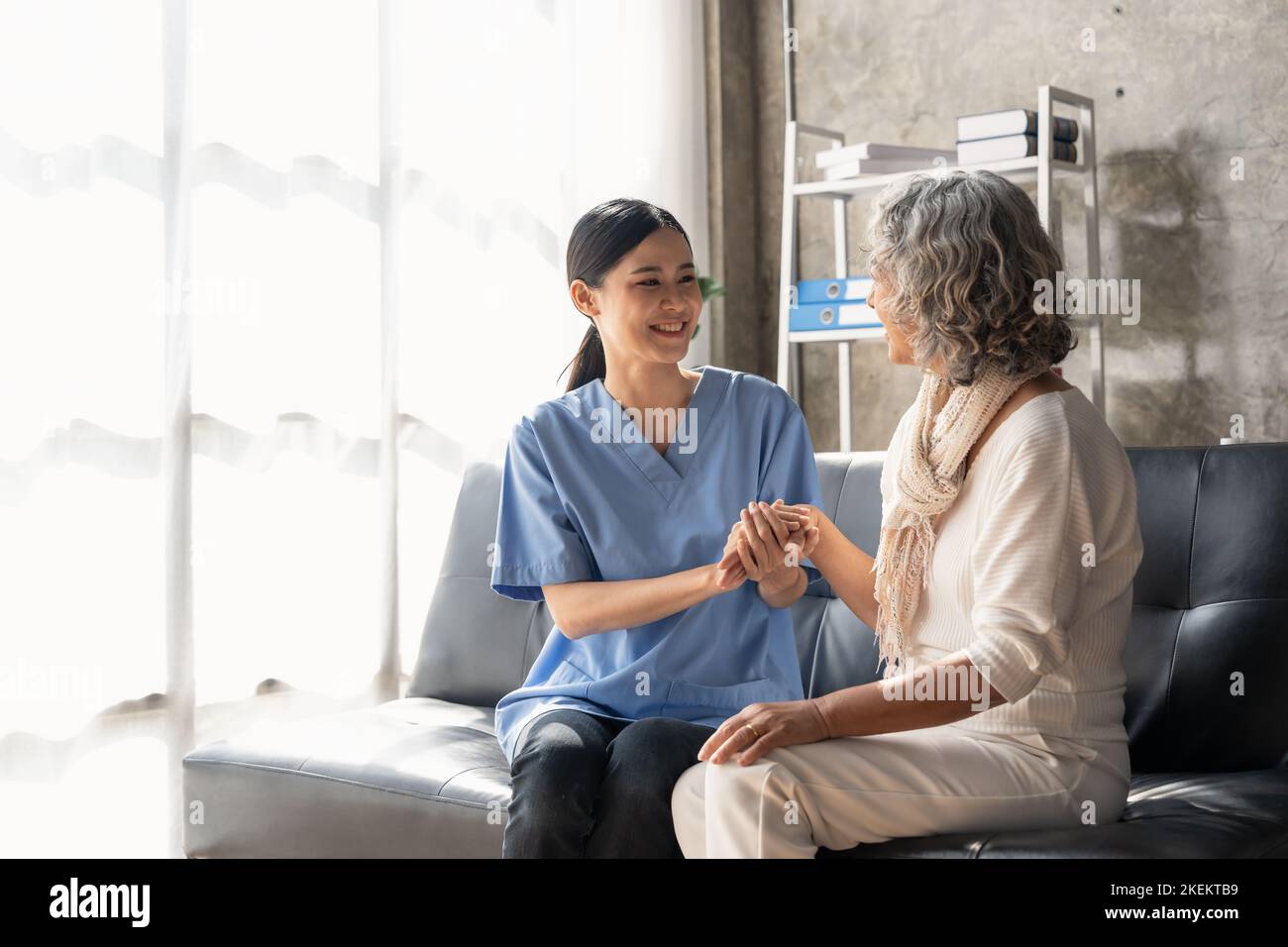 Ein glücklicher Patient hält die Pflegekraft an der Hand, während er Zeit miteinander verbringt. Ältere Frau im Pflegeheim und Krankenschwester. Stockfoto