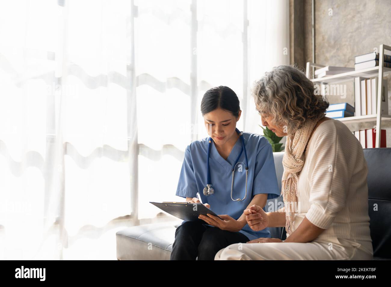 Ein glücklicher Patient hält die Pflegekraft an der Hand, während er Zeit miteinander verbringt. Ältere Frau im Pflegeheim und Krankenschwester. Stockfoto