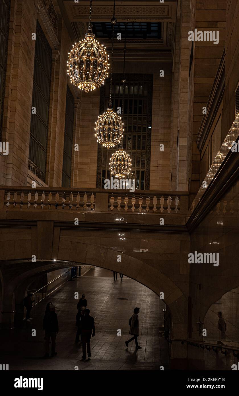 Vertikales Foto des beeindruckenden Grand Central Terminals mit hängenden Kristallkronleuchtern und zu Fuß fahrenden Passagieren. Stockfoto