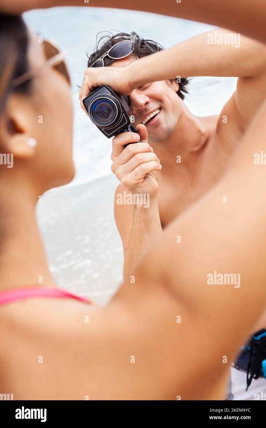 Mann und Frau Paar, Freund, der Videos macht oder seine Freundin in einem Bikini am Strand mit einer Retro-Cine-Filmkamera filmt Stockfoto