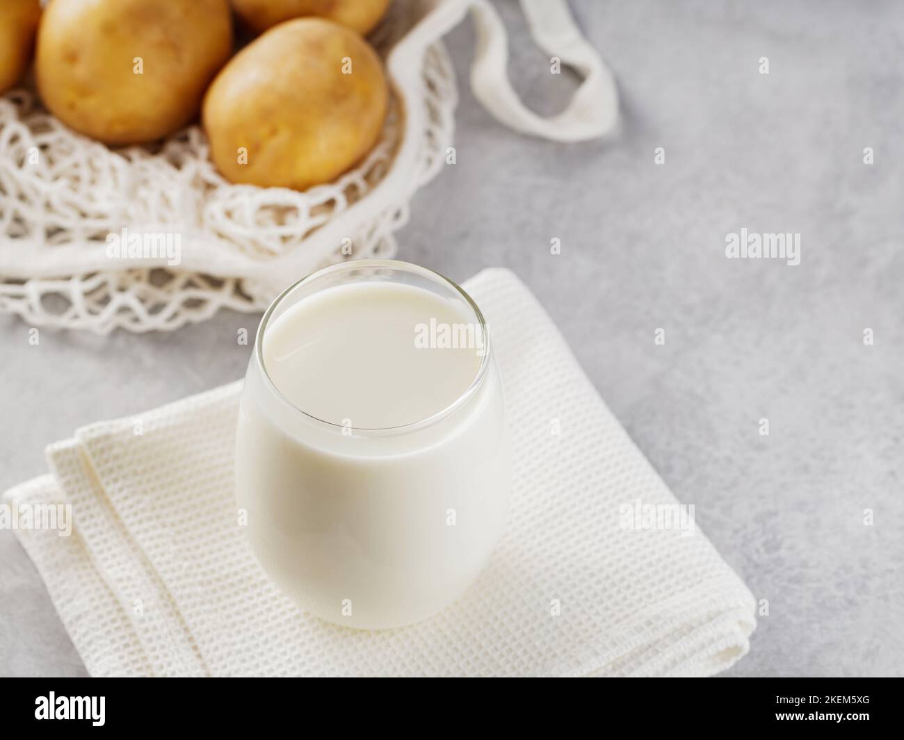 Kartoffelmilch und rohe Kartoffeln in einem Netzbeutel. Alternative Getränke ohne Milchprodukte und Zutaten auf grauem Hintergrund. Allergenfreies und Zero Waste Konzept. Oben Stockfoto