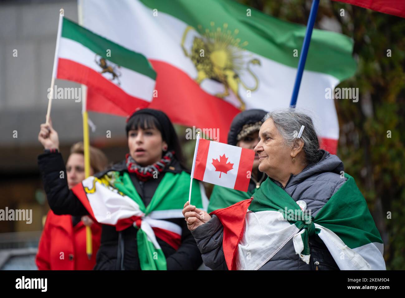 Eine ältere Frau mit einer iranischen shir-o-khorshid-Flagge trägt während einer Kundgebung in Toronto in Solidarität mit dem iranischen Volk eine kanadische Flagge. Stockfoto