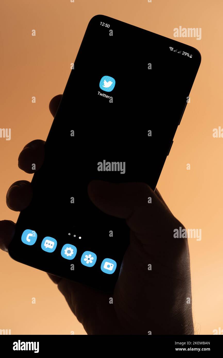 New york, USA - 4. November 2022: Öffnen sie die twitter-App auf dem Smartphone, halten Sie die Hand isoliert auf braunem Hintergrund Stockfoto