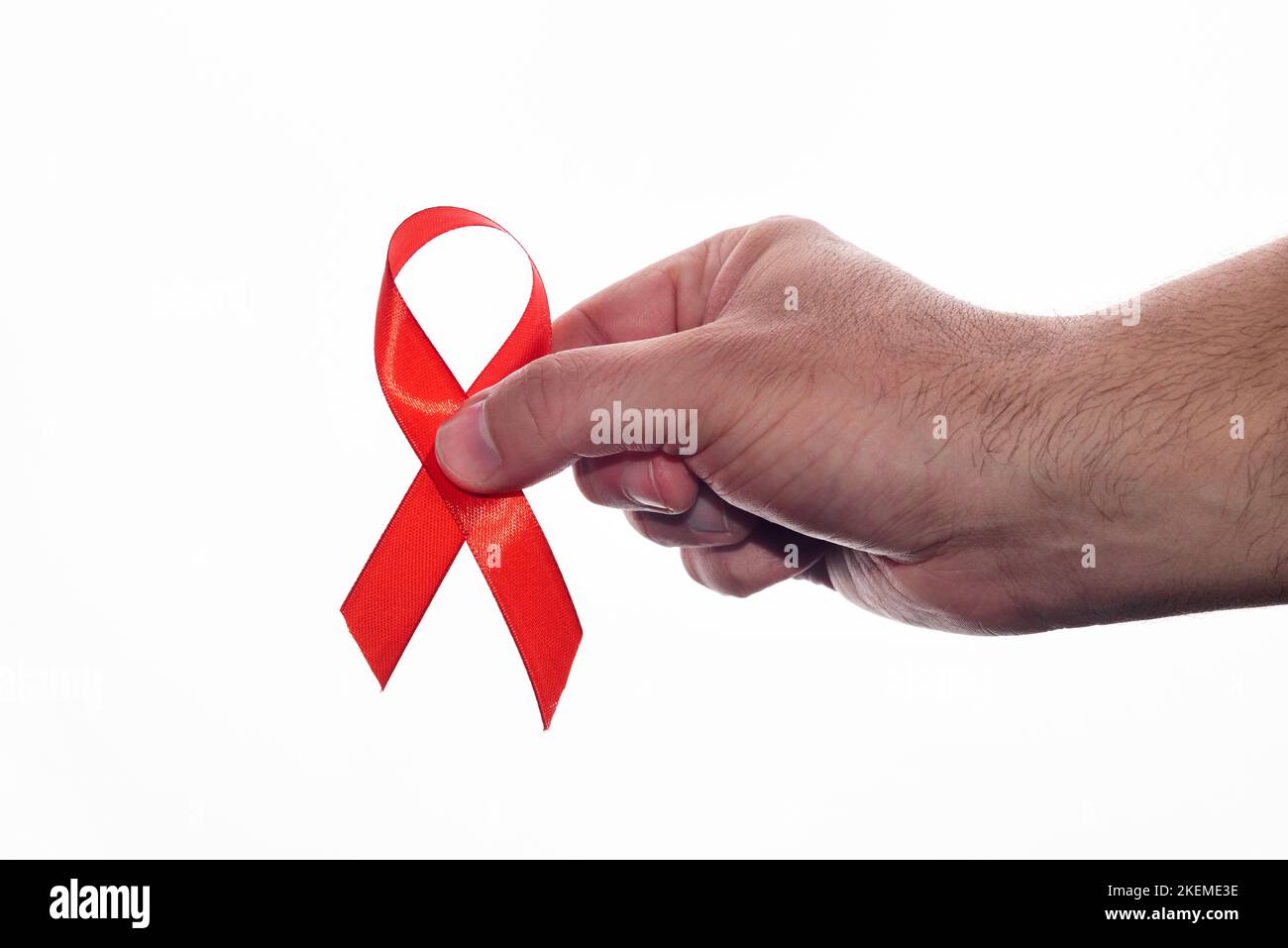 Die Hand eines Mannes, der ein rotes Band zur Unterstützung des Welt-AIDS-Tages auf weißem Hintergrund hält. 1. Dezember, hiv-Tag Stockfoto