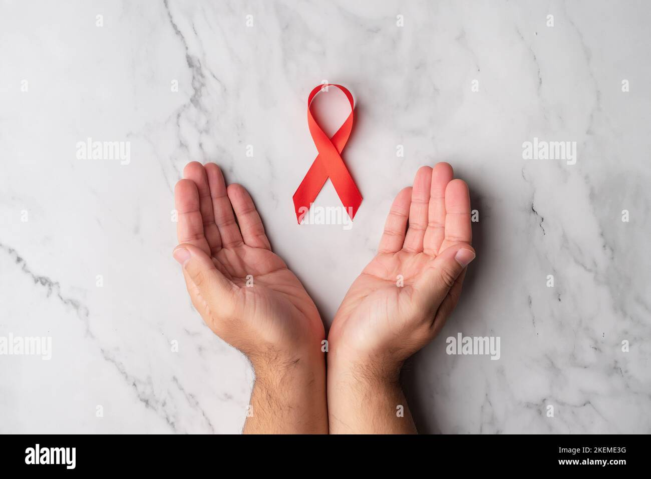 Die offenen Hände eines Mannes mit einem roten Band zur Unterstützung des Welt-AIDS-Tages. Verständnis mit Menschen, die mit hiv infiziert sind Stockfoto