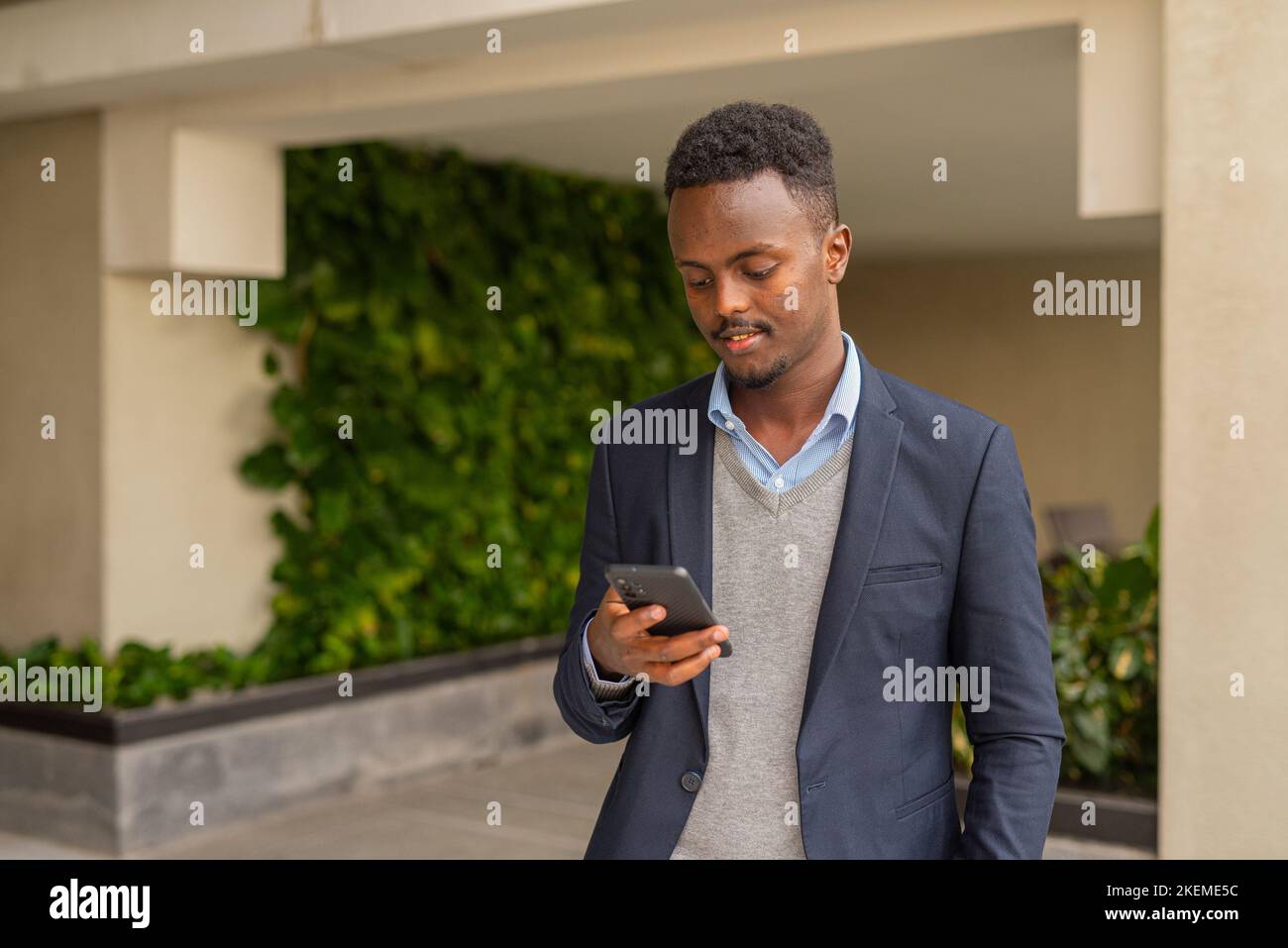 Porträt eines hübschen schwarzen afrikanischen Geschäftsmannes in Anzug und SMS mit Smartphone Stockfoto