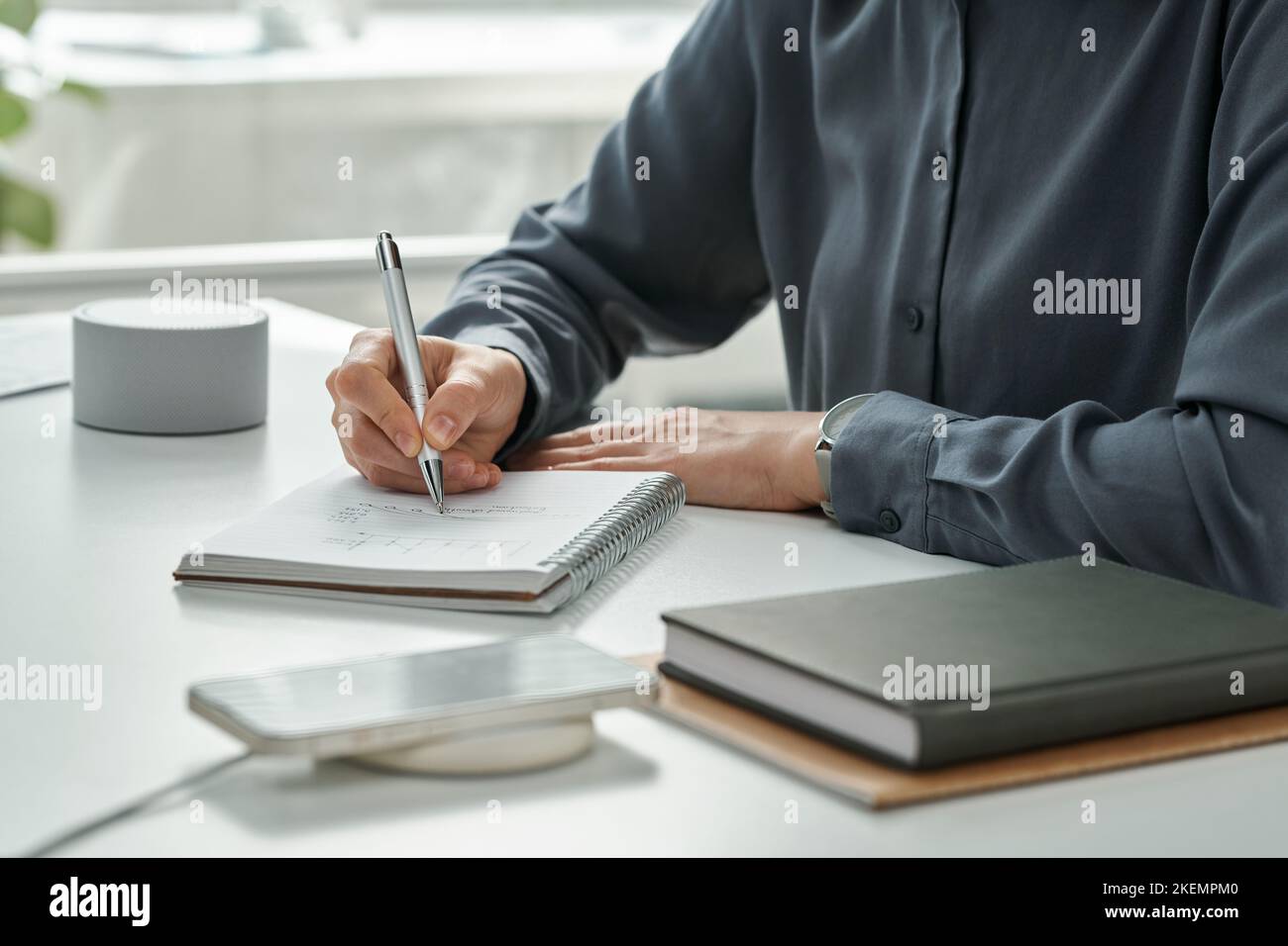 Nahaufnahme des Managers, der Pläne in Notizblock schreibt, während er mit modernen drahtlosen Geräten am Tisch sitzt Stockfoto
