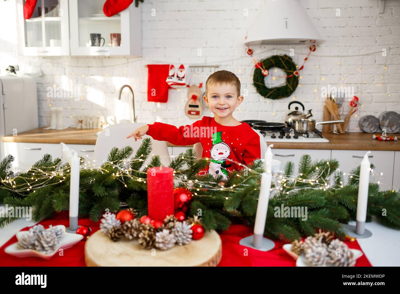 Ein Porträt eines Jungen, der in der Küche am Weihnachtstisch sitzt und für das neue Jahr dekoriert ist. Weihnachtsdekor in der Küche Stockfoto