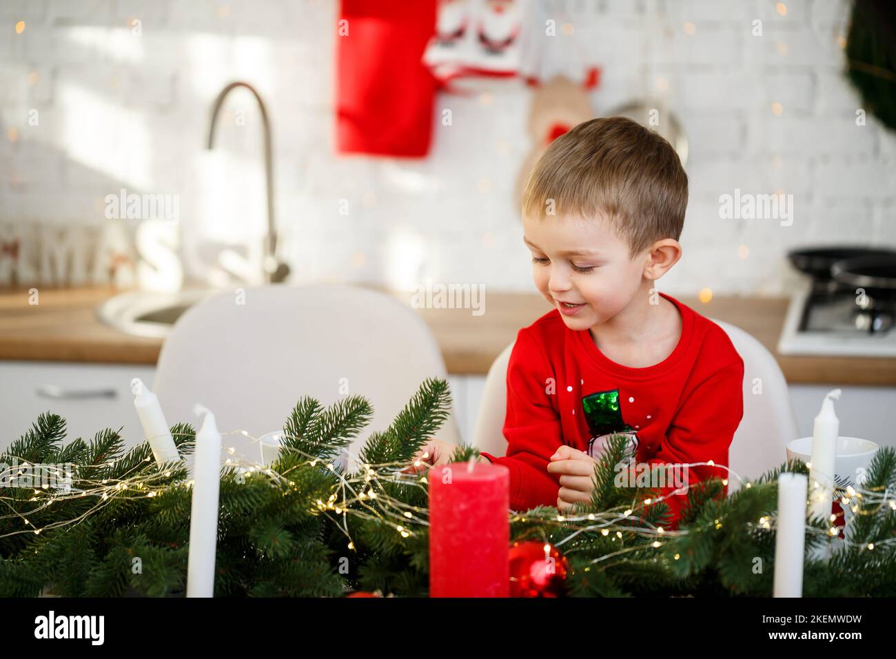 Ein Porträt eines Jungen, der in der Küche am Weihnachtstisch sitzt und für das neue Jahr dekoriert ist. Weihnachtsdekor in der Küche Stockfoto