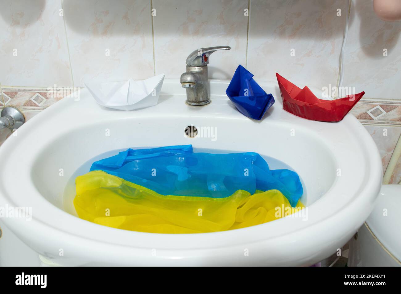 Die russische Flagge von Papierbooten schwebt auf dem Wasser auf den Flaggen der Ukraine im Waschbecken im Badezimmer, dem Krieg in der Ukraine mit Russland Stockfoto