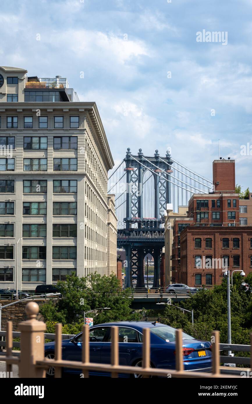 Manhattan Bridge zwischen Manhattan und Brooklyn über dem East River von einer schmalen Straße aus gesehen, die an sonnigen Tagen in New York von Gebäuden umgeben ist Stockfoto