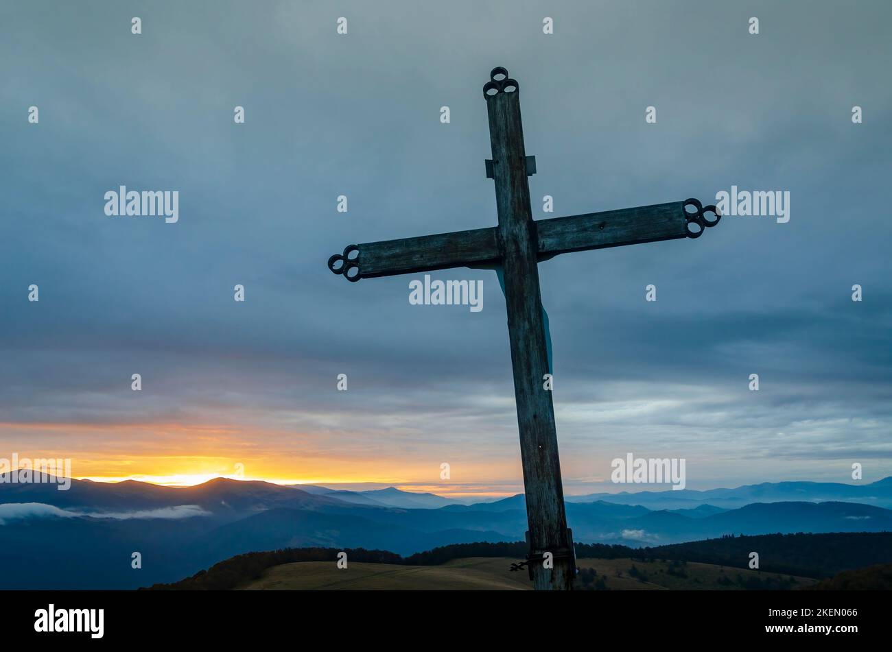 Geneigtes Kreuz mit dramatischem Sonnenuntergangshimmel hoch in den Bergen. Symbol der Hoffnung und des Christentums Stockfoto