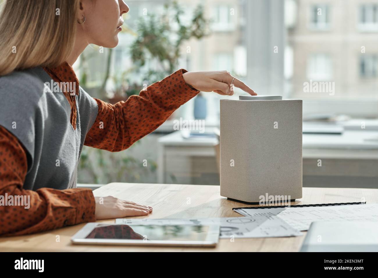 Junge Frau mit Smart Speaker und Beratung mit Online-Assistent während der Arbeit am Tisch im Büro Stockfoto