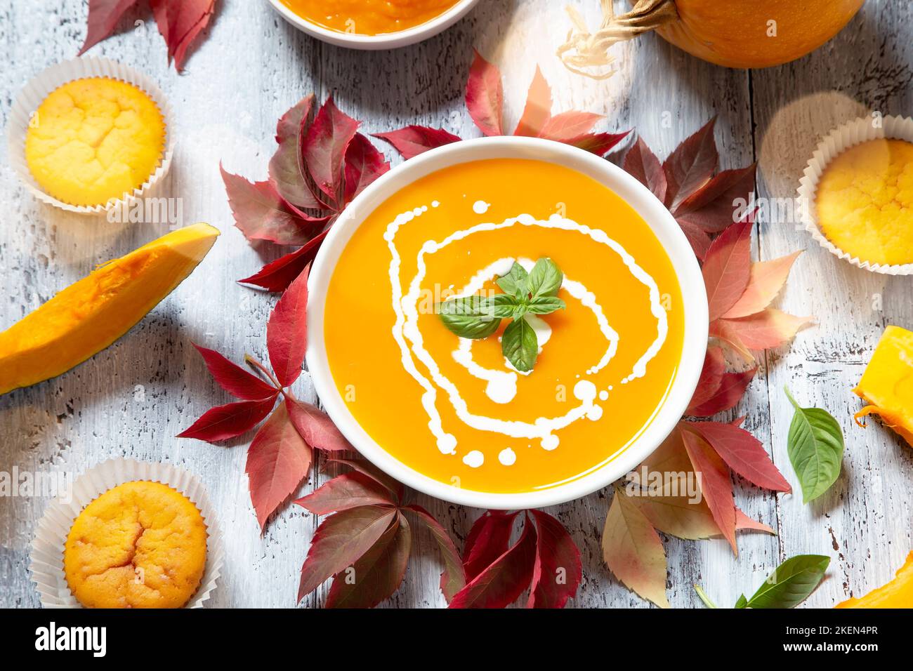 Kürbissuppe und Muffins mit dem trockenen Blätter im Herbst auf weißem Holz- Hintergrund Stockfoto