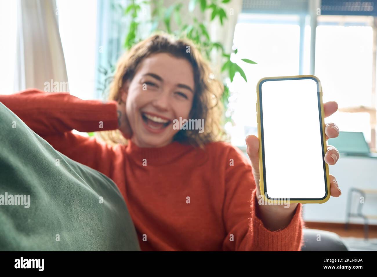 Glückliche junge Frau, die das Mobiltelefon in der Hand hält und den Bildschirm des Handymockup zeigt. Stockfoto