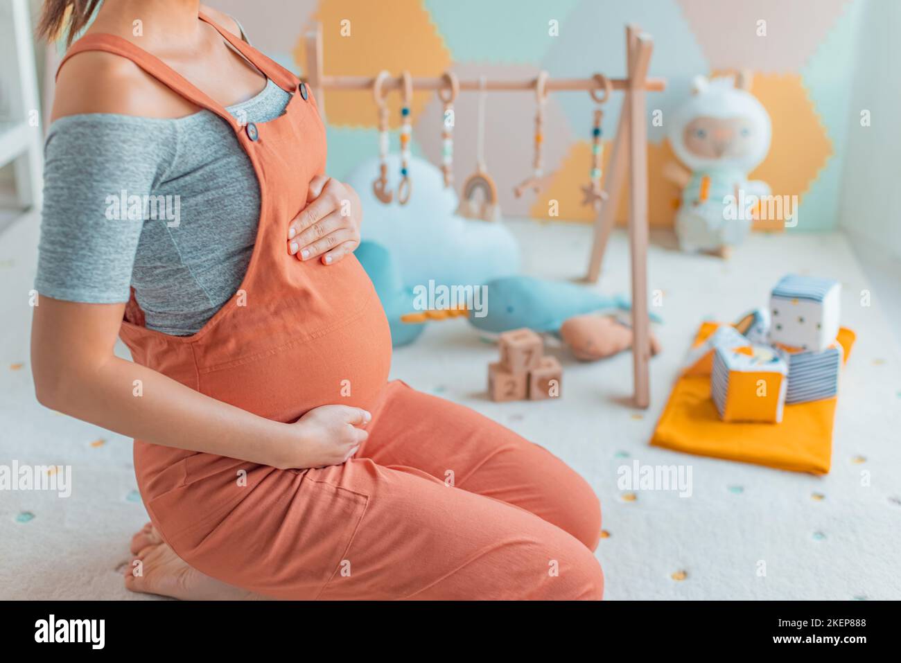 Schwangeren Bauch mit Baby-Aktivität Turnhalle Spiel, Spielzeug und Spielmatte in Kinderzimmer oder Spielzimmer. Schwangerschaftskonzept und Heimtextilien Stockfoto