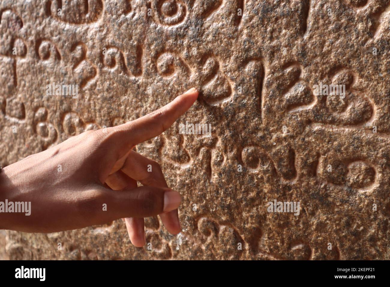 Der Zeigefinger eines Mannes zeigt die alte tamilische Schrift, die an der Wand des Tanjore Brihadeeswarar-Tempels geschnitzt wurde. Stockfoto