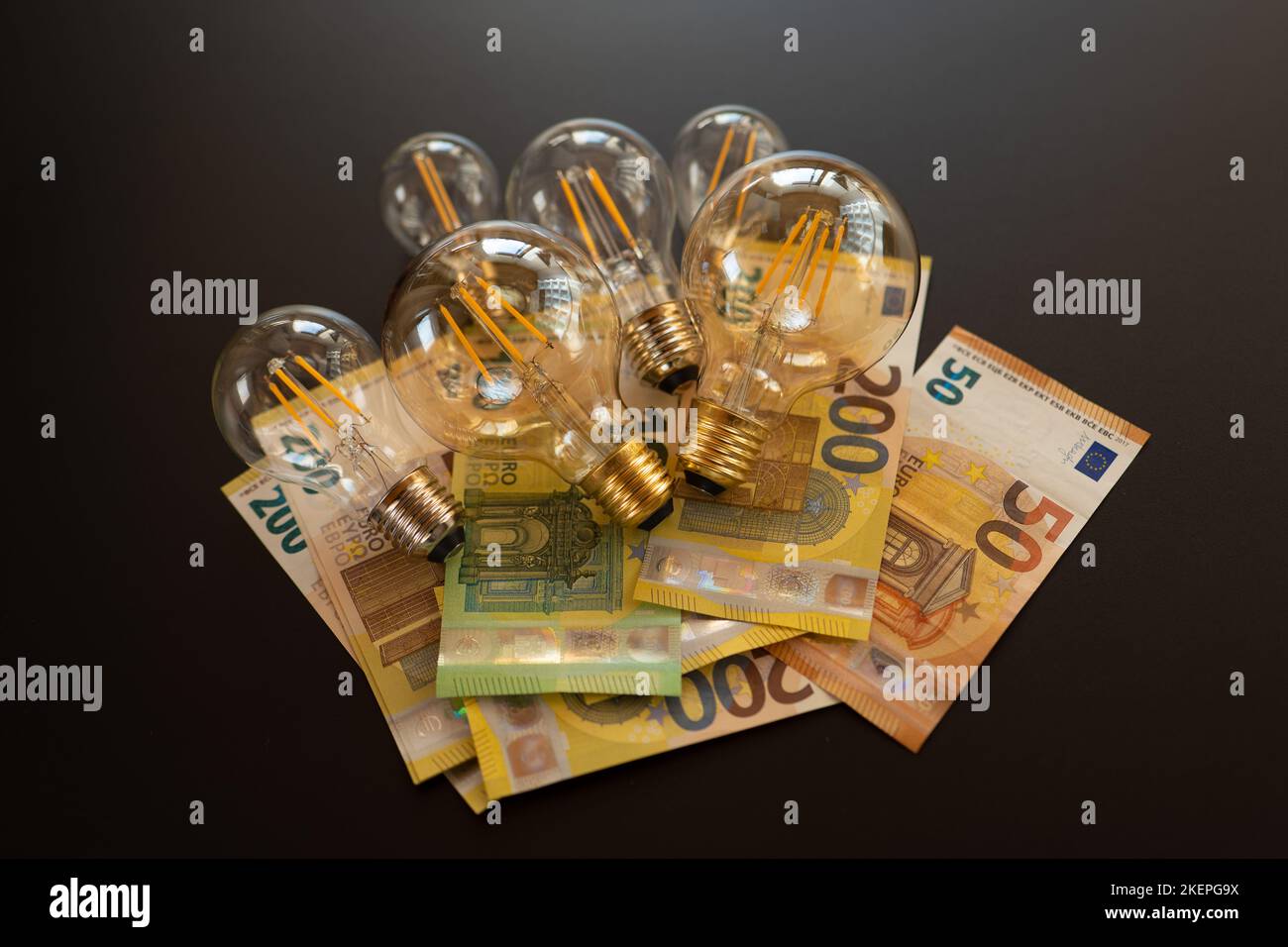 Glühbirnen und Euro-Banknoten auf schwarzem Hintergrund.Krise im Energiesektor.Zahlung der Stromkosten. Strompreis in Europa. Stockfoto