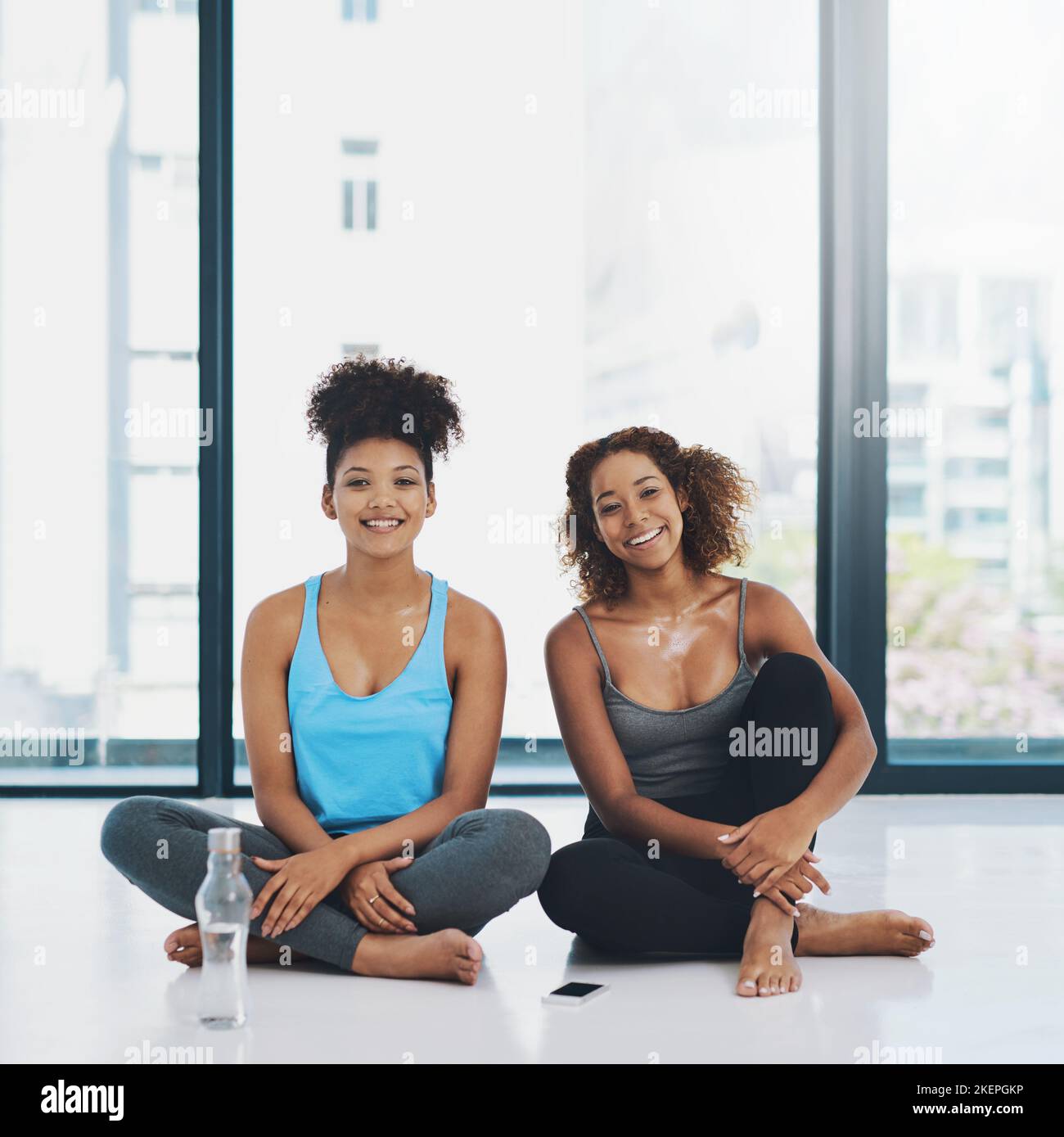 Eine kleine Pause machen. Portraitaufnahme von zwei jungen, fitfitfrauen Frauen, die sich auf dem Boden niedersetzen und vor einer Yoga-Sitzung in einem Studio ein Gespräch führen. Stockfoto
