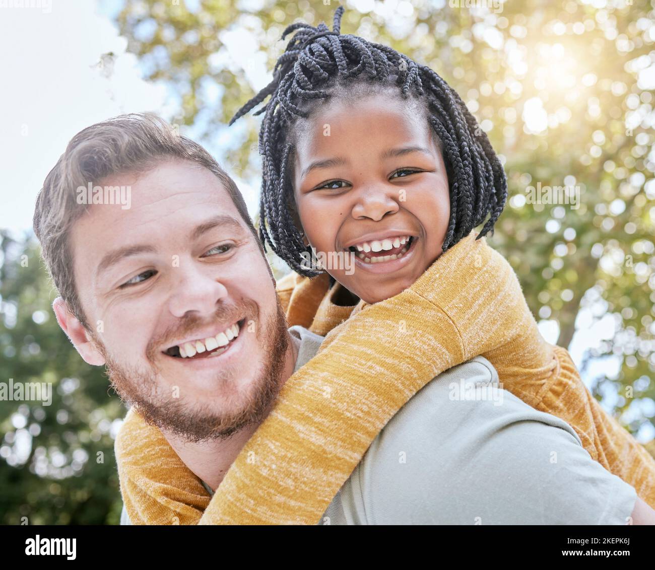 Park, Huckepack und Vater mit Mädchen Kind in der Natur spielen, verbinden und erkunden mit Bokeh. Glücklich, Lächeln und Porträt eines interracial Kind mit Stockfoto