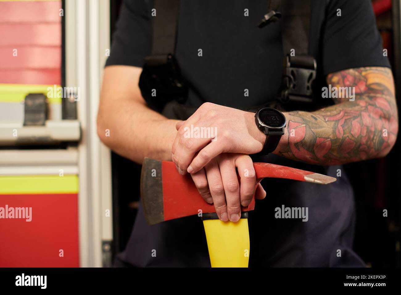 Junge gut aussehende Erwachsene, muskulöse Feuerwehrmann in Uniform hält Axt Feuer Ausrüstung in den Händen, isoliert auf LKW-Hintergrund. Stockfoto