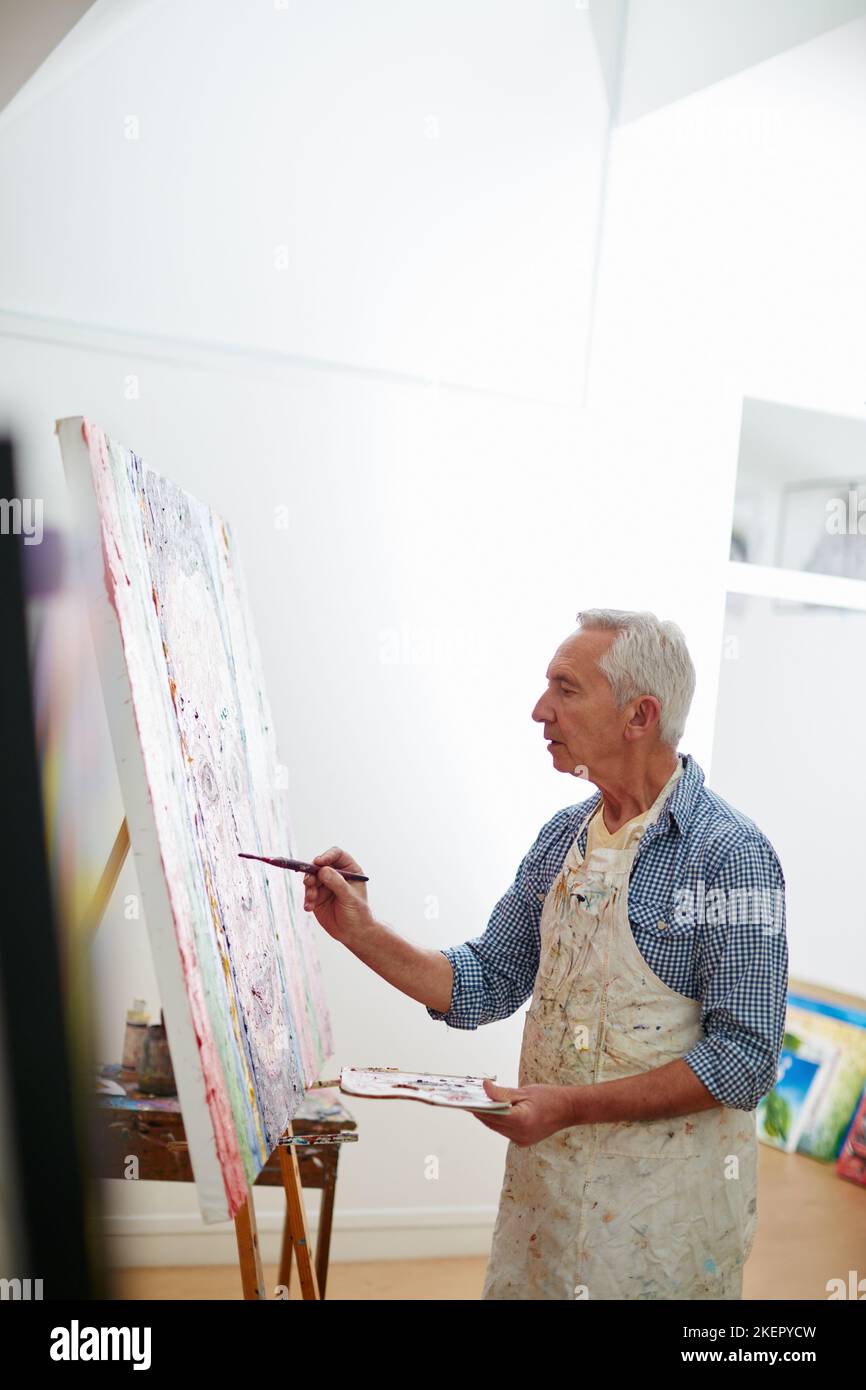 Kreativität ist ein wilder Geist und ein fokussiertes Auge. Ein älterer Mann, der zu Hause an einem Gemälde arbeitet. Stockfoto