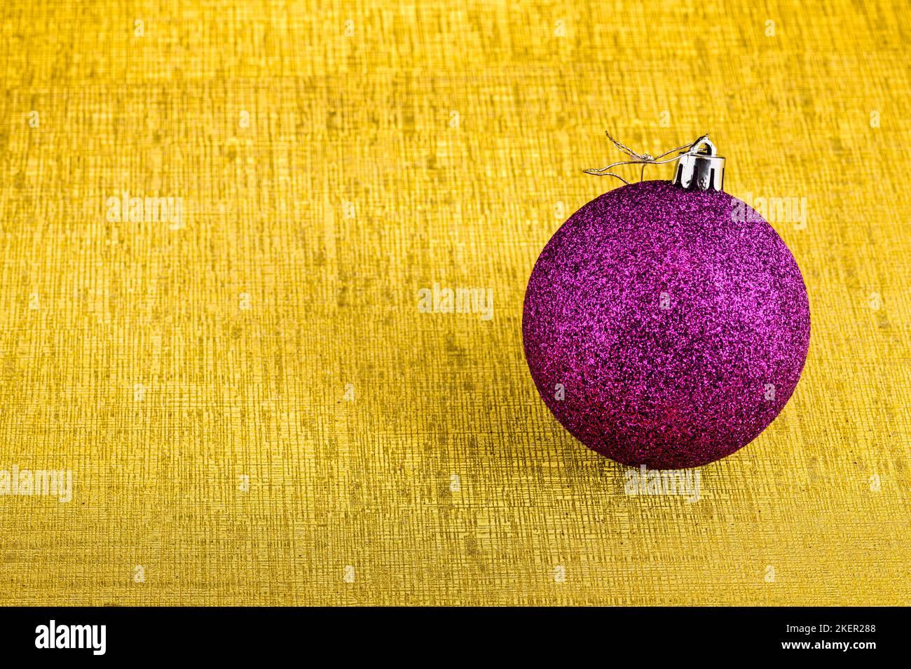 Eine lila weihnachtskugel mit Glitzer isoliert auf einem goldenen Hintergrund mit Textur. Stockfoto