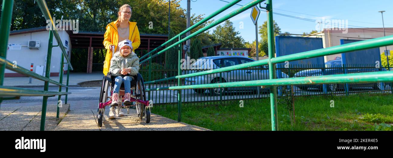 Die junge Mutter schob mit ihrer Tochter, die mit einer zerebralen Lähmung lebt, einen Rollstuhl auf den Weg zur Therapie. Barrierefreier Zugang, Rollstuhl oder Push Stockfoto