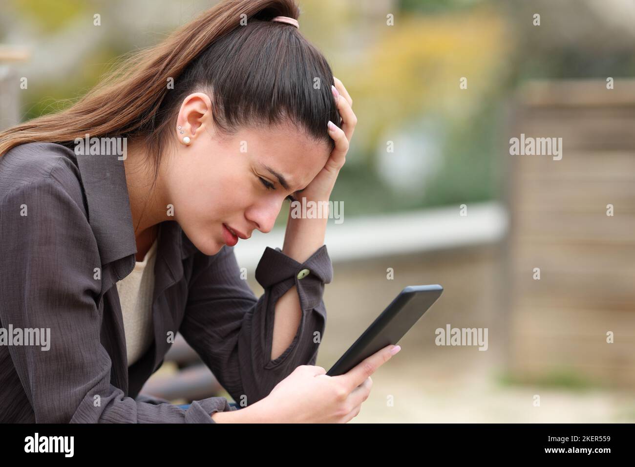 Beunruhigte Teenager beschwerten sich beim Überprüfen schlechter Nachrichten auf dem Handy in einem Park Stockfoto