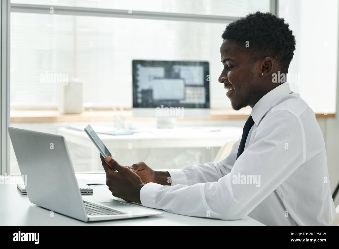 Der junge afroamerikanische Geschäftsmann, der an seinem Arbeitsplatz im Büro drahtlose Geräte verwendet, arbeitet online an einem digitalen Tablet Stockfoto