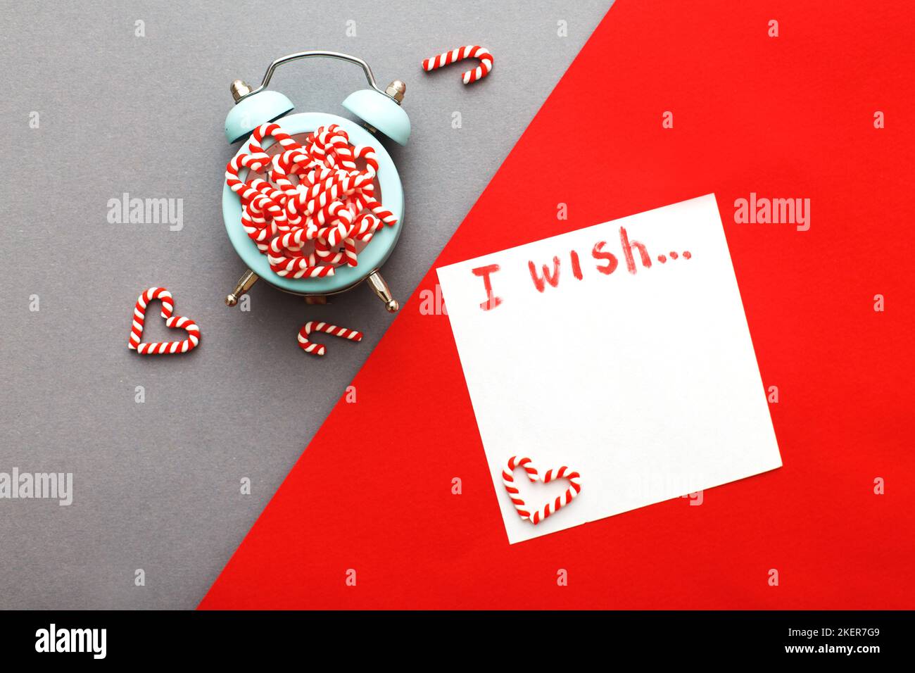 Weihnachtshintergrund mit Zuckerstöcken mit Wecker auf blaugrauem und rotem Hintergrund. Stockfoto