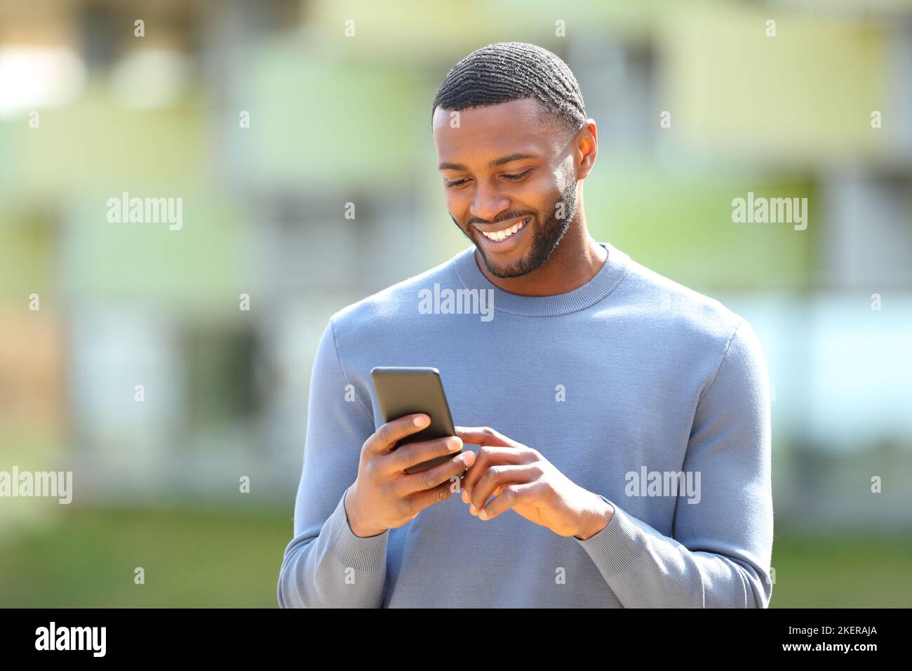 Ein glücklicher schwarzer Mann überprüft das Handy, das auf der Straße läuft Stockfoto