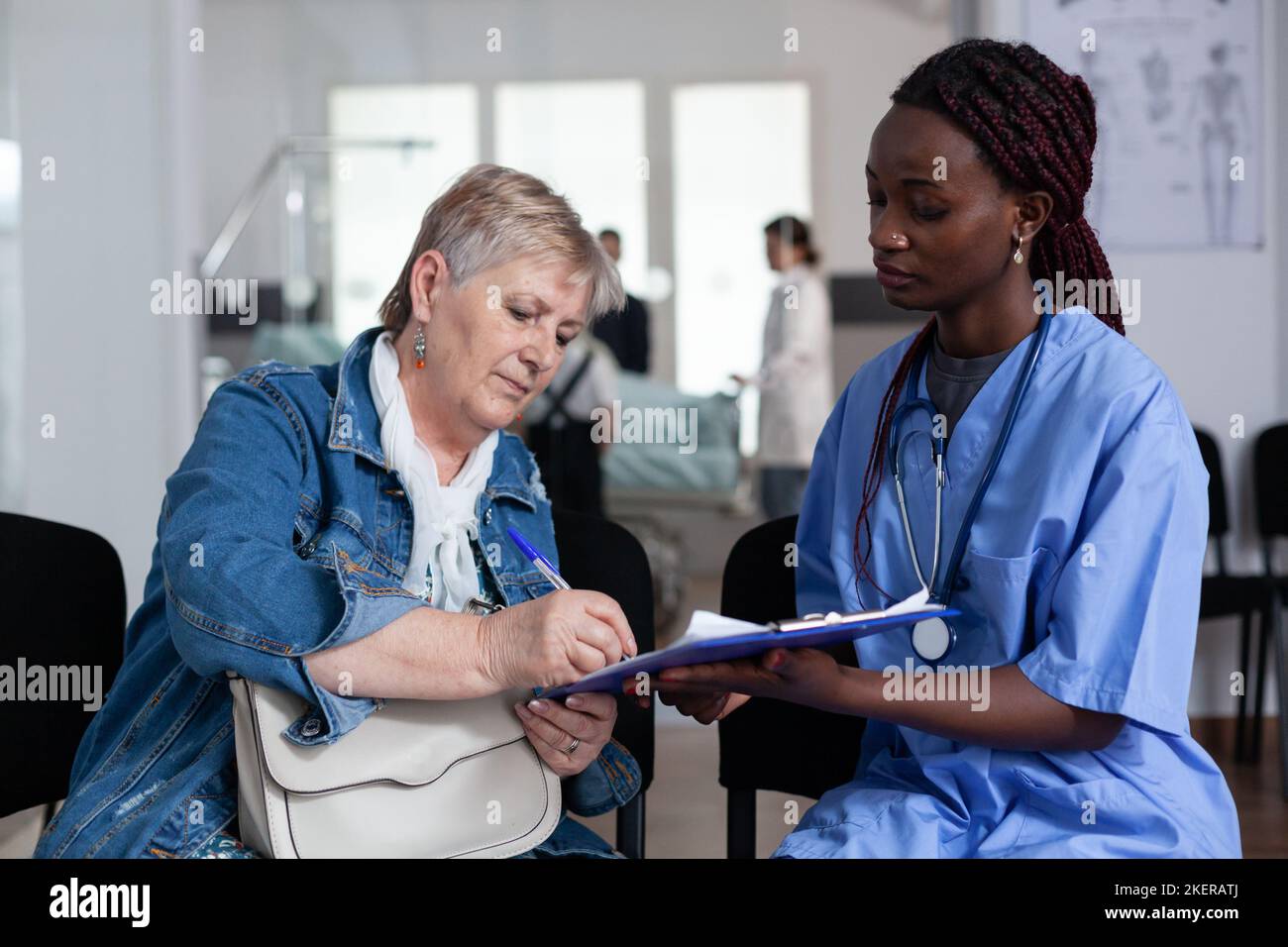 Ältere kaukasische Frau, die Entlassungspapiere im Bereich des geriatrischen Krankenhausausgangs unterschrieb. Afro-Krankenschwester, die eine alte Dame an der Klinikrezeption besucht. Leitender Patient, der medizinische Dokumente ausfüllt. Stockfoto