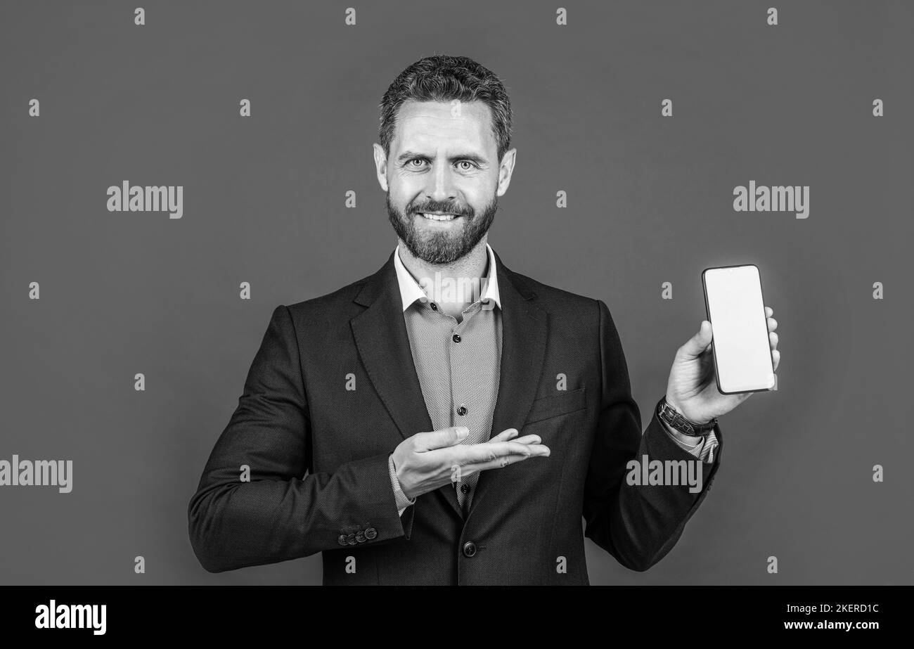 Reifer fröhlicher Mann Geschäftsmann in Anzug präsentiert Produkt von Smartphone, Copy Space, Werbung. Stockfoto