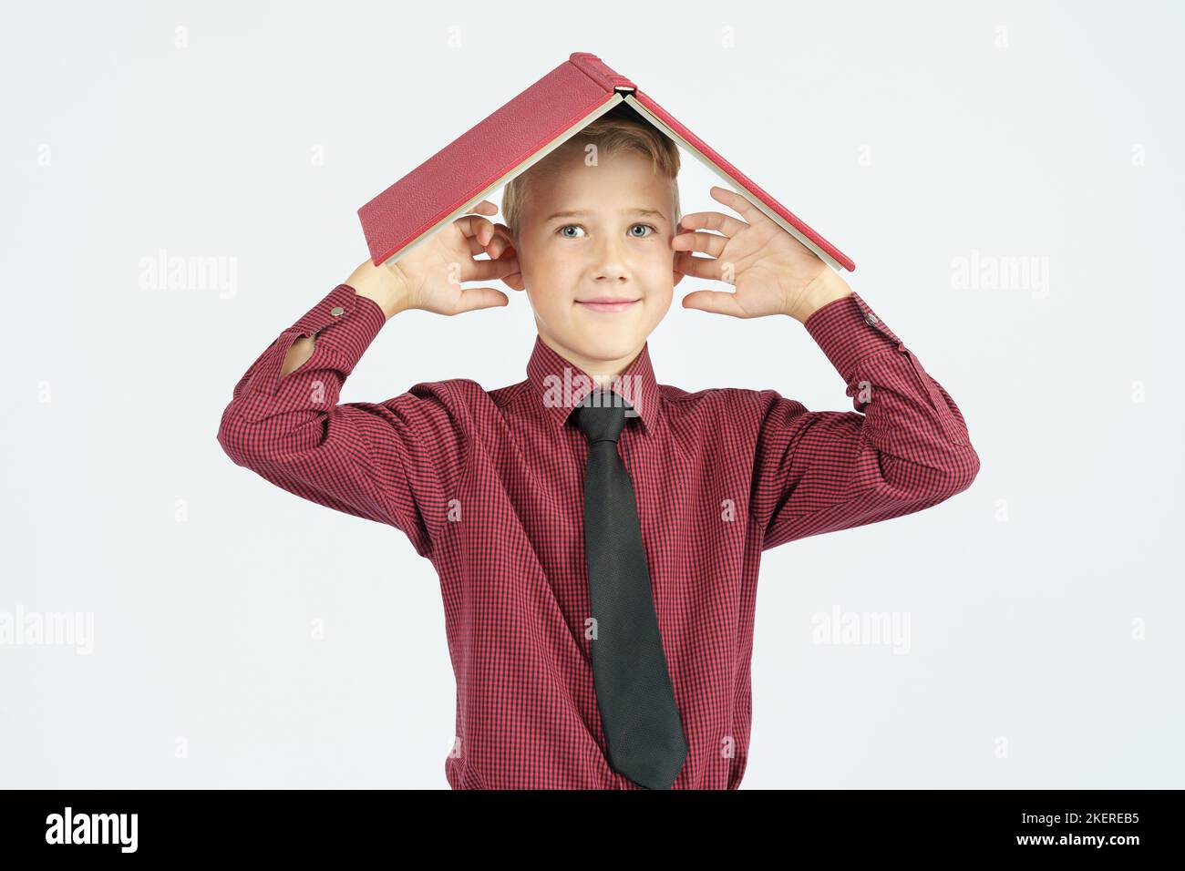 Der Schuljunge legte ein offenes Buch auf seinen Kopf und bedeckte seine Ohren mit den Fingern, isolierter Hintergrund. Bildungskonzept Stockfoto