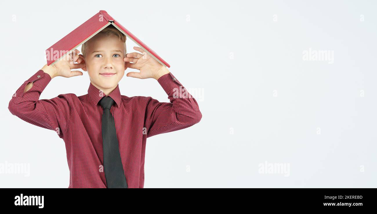 Der Schuljunge legte ein offenes Buch auf seinen Kopf und bedeckte seine Ohren mit den Fingern, isolierter Hintergrund. Bildungskonzept Stockfoto