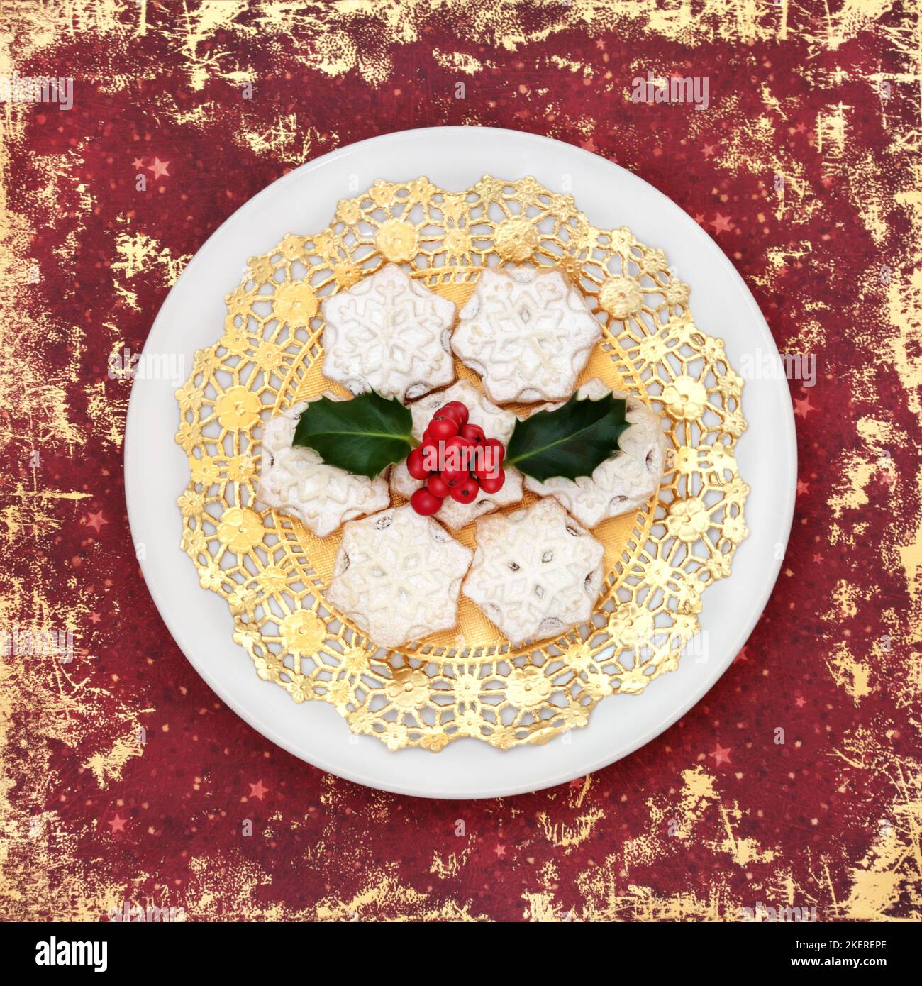 Hausgemachte Weihnachtsgebäck mit Winterholly auf weißem Teller und rotem Grunge-Hintergrund. Festliches Design für traditionelle Speisen zu Weihnachten und Neujahr. Stockfoto